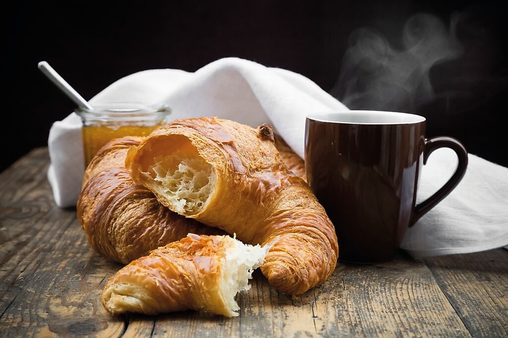 Croissant with coffee and honey on a wooden table.