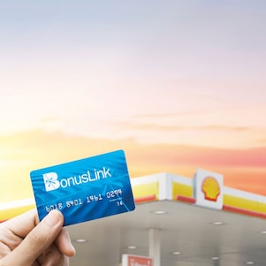 Hand holding a bonus link card with Shell station in the background