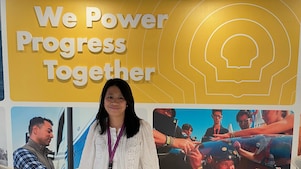 Person standing before a Shell display with the message “We Power Progress Together” and photos of employees and teamwork