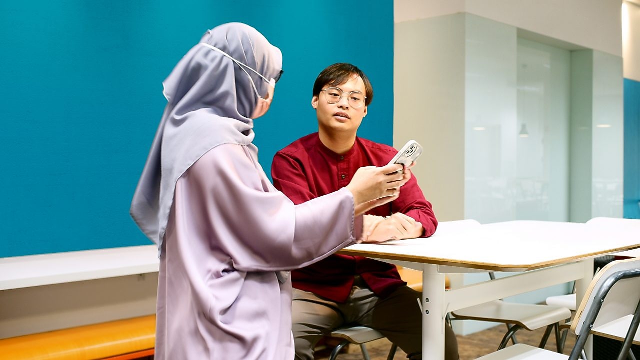 Badrul talking to his colleague and discussing that the colleague is showing on her phone.