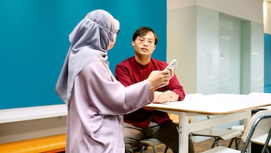 Badrul talking to his colleague and discussing that the colleague is showing on her phone.