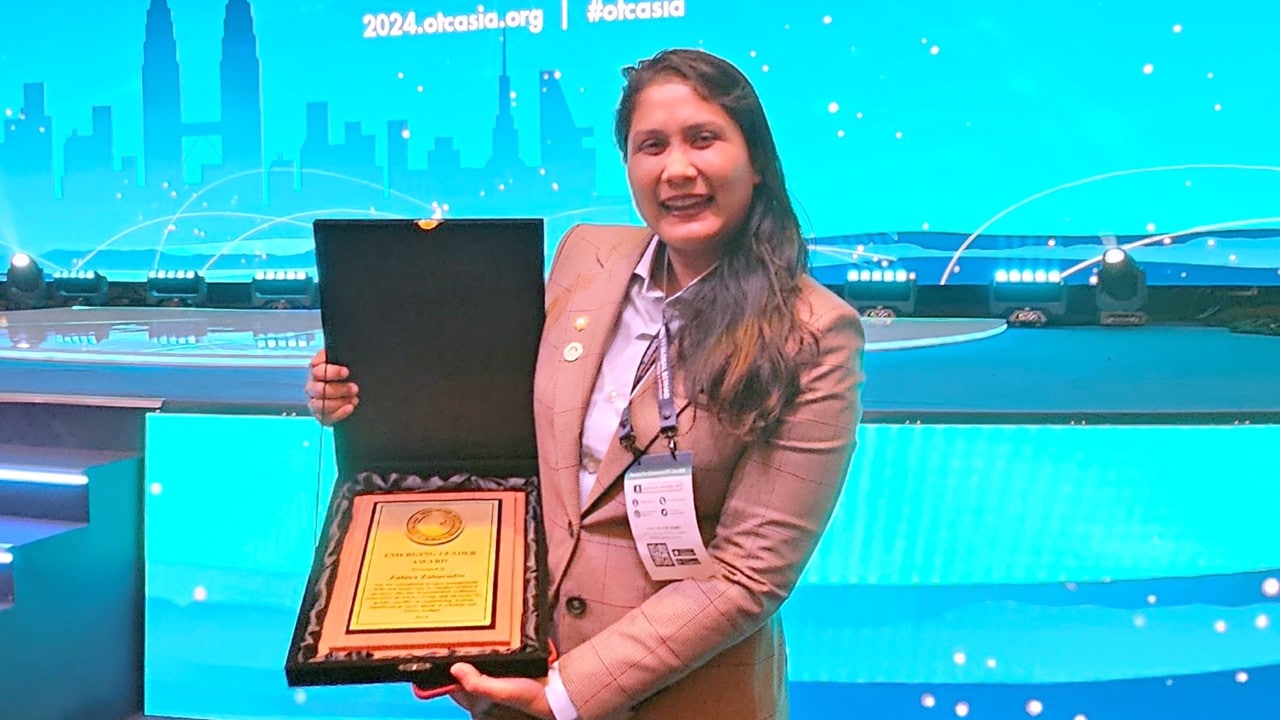 Zahira posing with the awards plate and standing in front of the awards stage