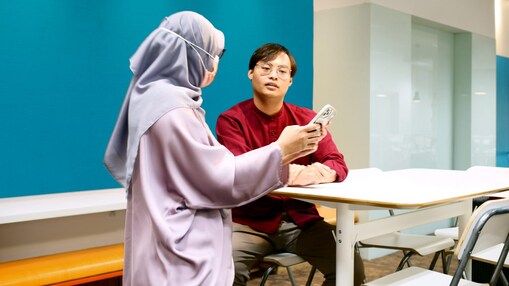 Badrul talking to his colleague and discussing that the colleague is showing on her phone.