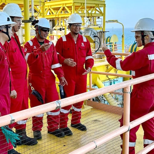 A female engineer in discussion with her team at an offshore site, with all of them equipped with coveralls and safety helmets.
