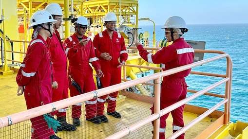A female engineer in discussion with her team at an offshore site, with all of them equipped with coveralls and safety helmets.
