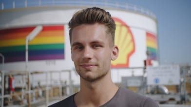 A male Shell employee standing in front of a refinery with rainbow colors