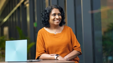 Featuring Subha in this image with her laptop in front of her while she smiles.