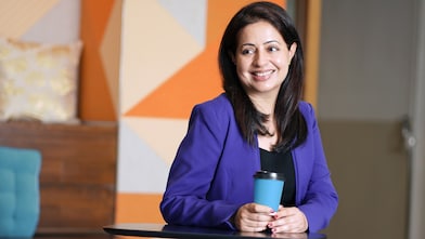 Simren smiling while look elsewhere with a closed coffee mug in front of her.
