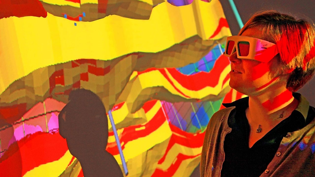 A woman with special goggles examines a 3D wall projection of a geological map