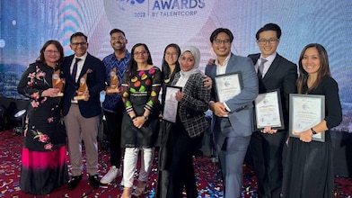 A group of Shell HR Professionals posing and smiling directly to the camera on stage holding the trophies and plaques received for the 4 awards