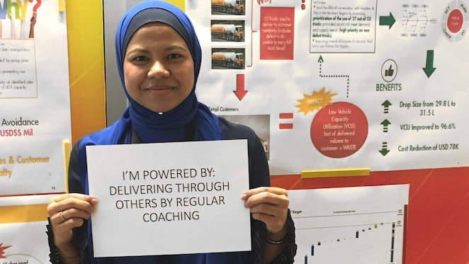 Maria holding a sign that reads ‘i’m powered by: delivering through others by regular coaching’