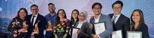 A group of Shell HR Professionals posing and smiling directly to the camera on stage holding the trophies and plaques received for the 4 awards