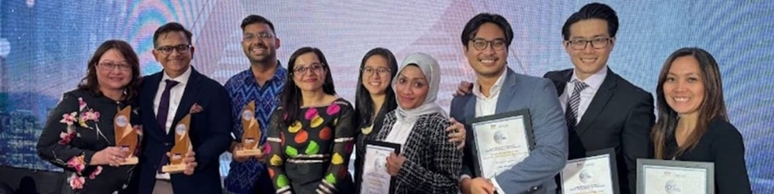 A group of Shell HR Professionals posing and smiling directly to the camera on stage holding the trophies and plaques received for the 4 awards