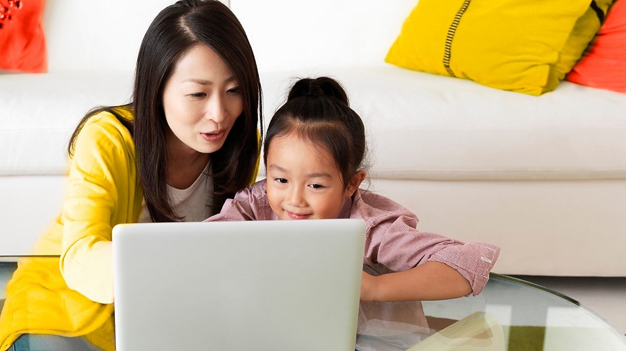 Older woman sitting with child at coffee table, looking at a tablet.