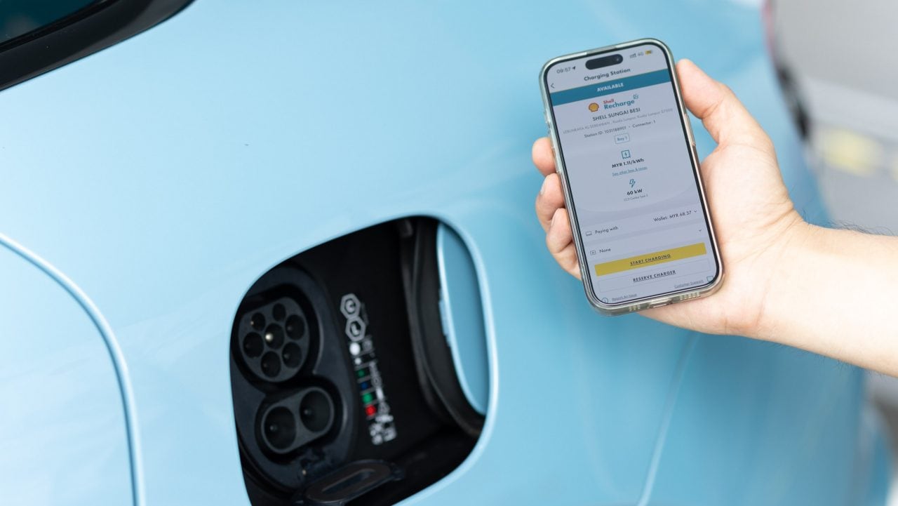 The new Shell Recharge App being displayed on a mobile phone next to an EV charging port