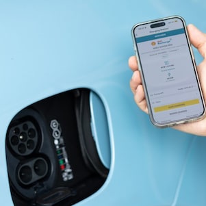 The new Shell Recharge App being displayed on a mobile phone next to an EV charging port