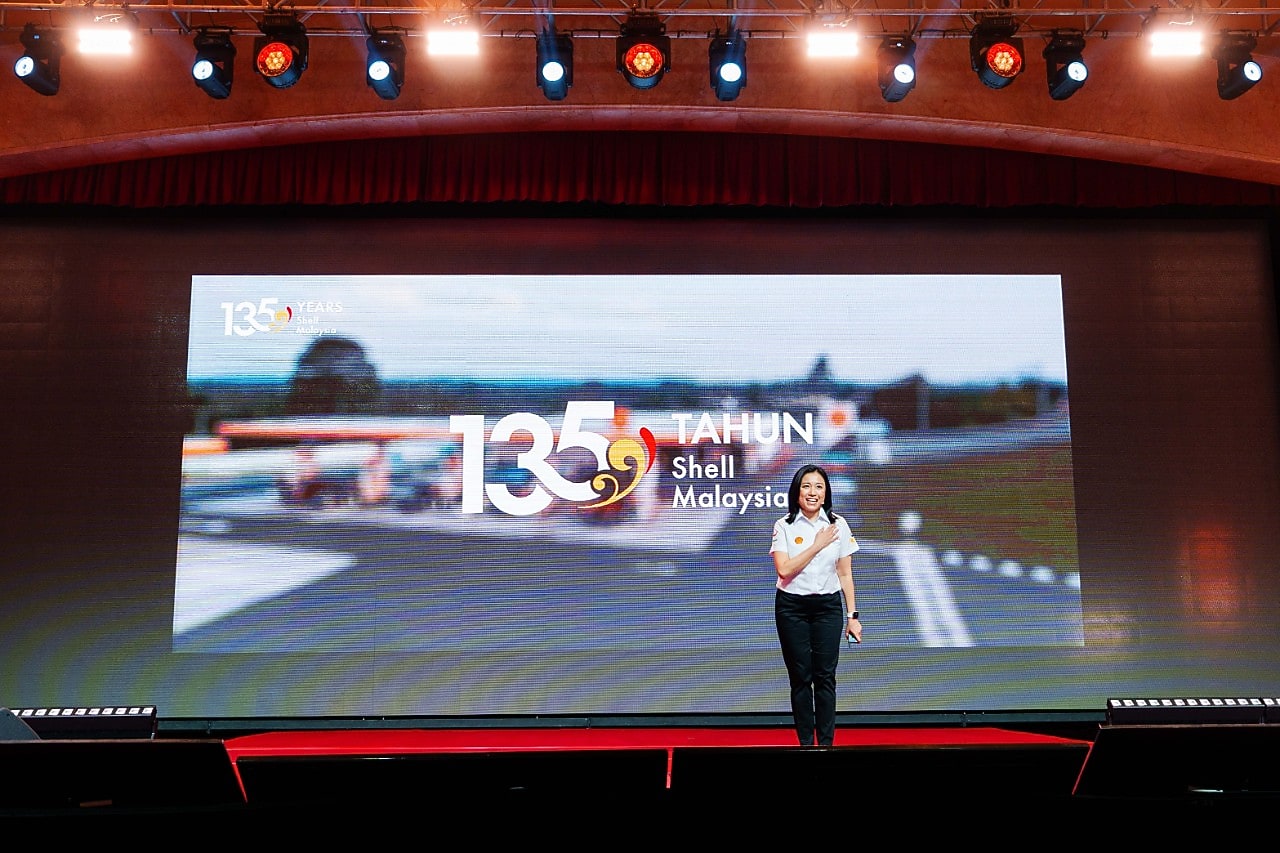 A Shell Malaysia representative speaks on stage in front of a large screen displaying the “135 Tahun Shell Malaysia” anniversary visual.