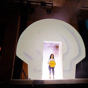 A Shell Malaysia representative makes a stage entrance through a lit Shell pecten backdrop, holding the Shell logo during the 135th anniversary media launch.