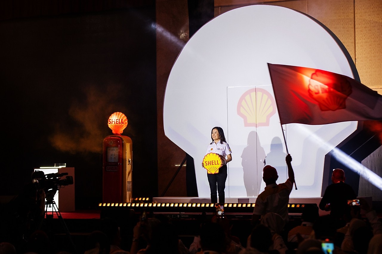 A Shell Malaysia representative stands centre stage holding the Shell logo, framed by a dramatic Shell pecten backdrop and stage lighting during the 135th anniversary launch.