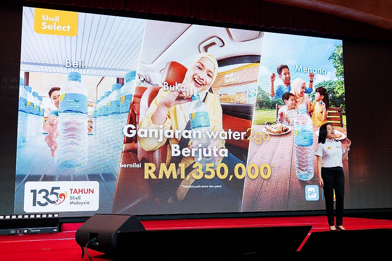 A presentation screen highlights the “Ganjaran water2go Berjuta” campaign and RM1.35 million in prizes, as a Shell representative presents the initiative on stage.
