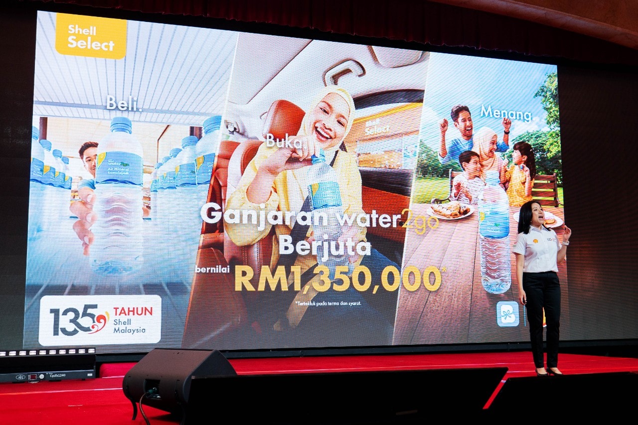 A presentation screen highlights the “Ganjaran water2go Berjuta” campaign and RM1.35 million in prizes, as a Shell representative presents the initiative on stage.