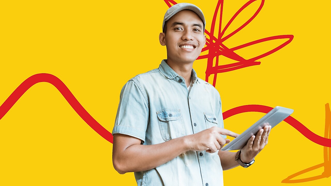 Young male entrepreneur smiling while holding an Ipad standing in front of the Shell LiveWIRE Malaysia 2022 graphical background