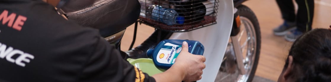 Shell Advance team pouring Shell Advance AX7 lubricant into Honda EX5 motorcycle during product demonstration.