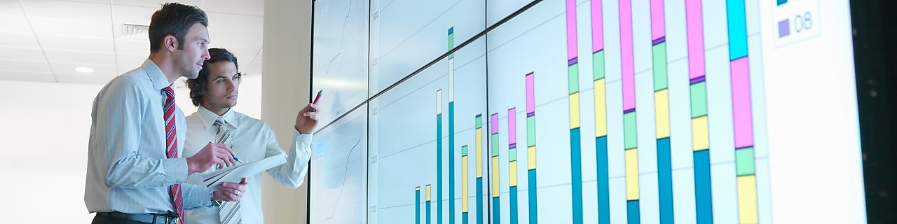 Business men analyse reports displayed on a large digital screen