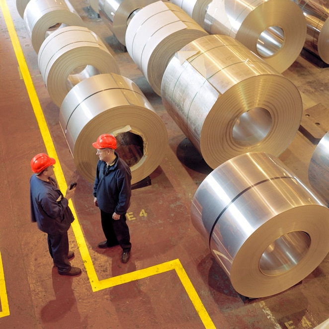 two factory workings talking next to large rolls of steel
