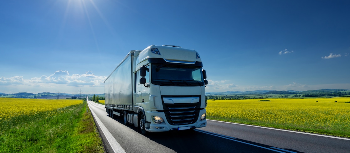 A large goods vehicle on the road between a field of yellow crops