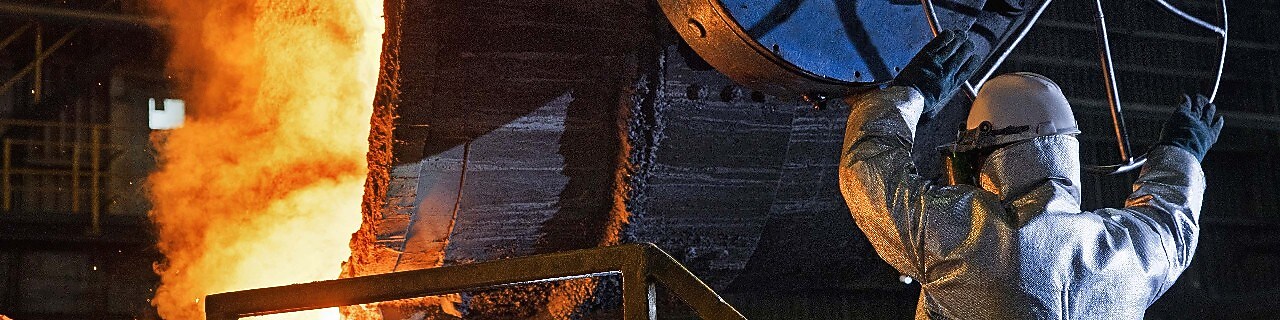 Two factory workers talking next to large rolls of steel