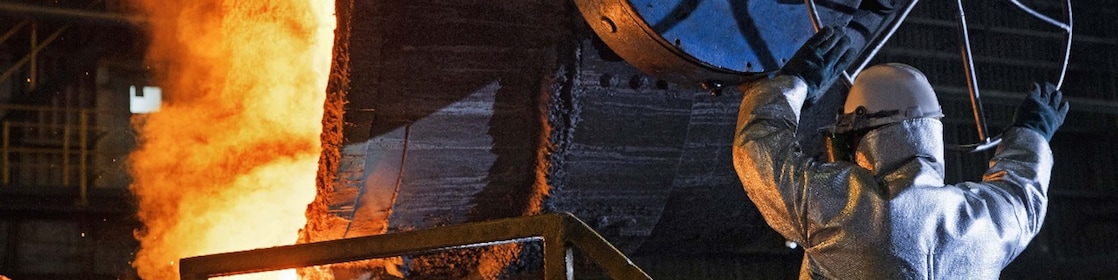 Two factory workers talking next to large rolls of steel