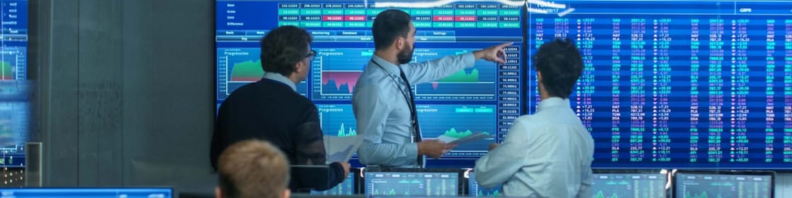 Three Experienced Stock Traders Talking Business, Consulting Documents and Argue About Data. They Work for a Big Stock Exchange Firm. Office is Full of Displays Showing Infographics and Numbers.