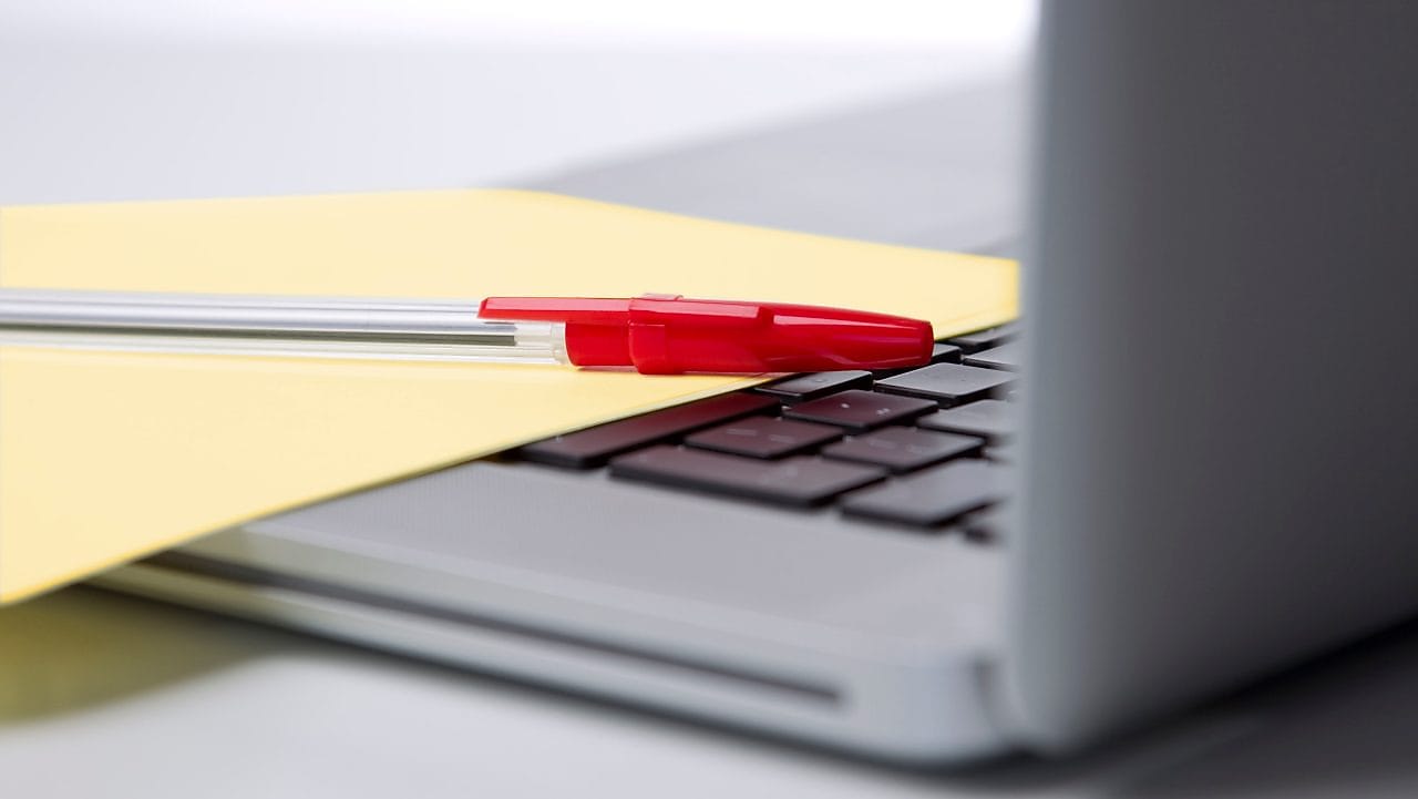 Photo of red pan on yellow piece of paper, placed on the keyboard of a laptop