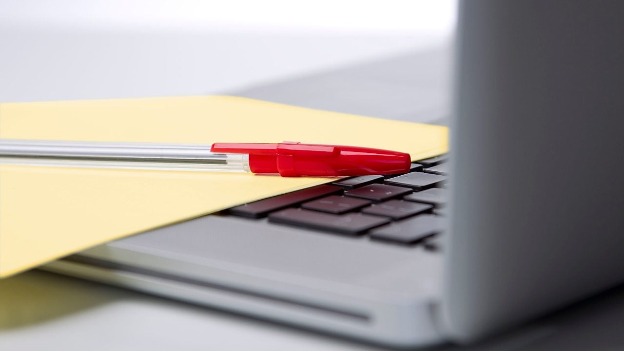 Photo of red pan on yellow piece of paper, placed on the keyboard of a laptop
