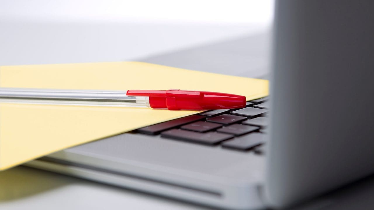 Photo of red pan on yellow piece of paper, placed on the keyboard of a laptop