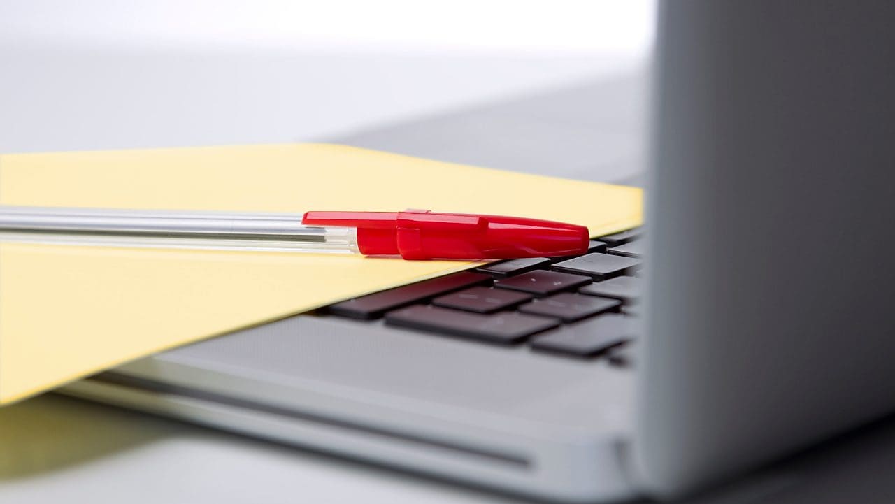 Photo of red pan on yellow piece of paper, placed on the keyboard of a laptop