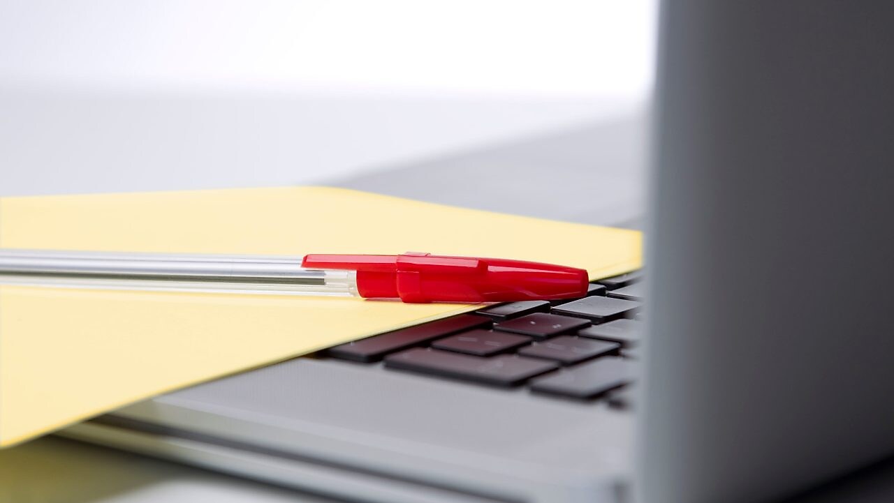 Photo of red pan on yellow piece of paper, placed on the keyboard of a laptop