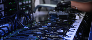 A gloved hand next to an assortment of wires connecting to a computer system.