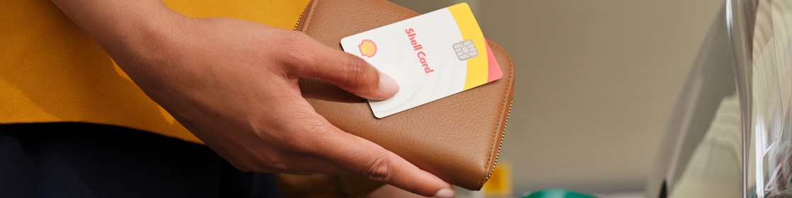  Female Shell customer holding a Shell card and purse while refueling on a Shell forecourt.