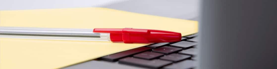 Pen and paper on a laptop