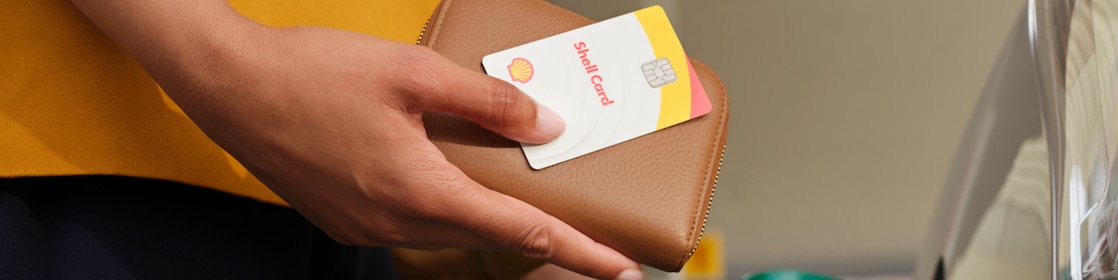 Female Shell customer holding a Shell card and purse while refueling on a Shell forecourt.