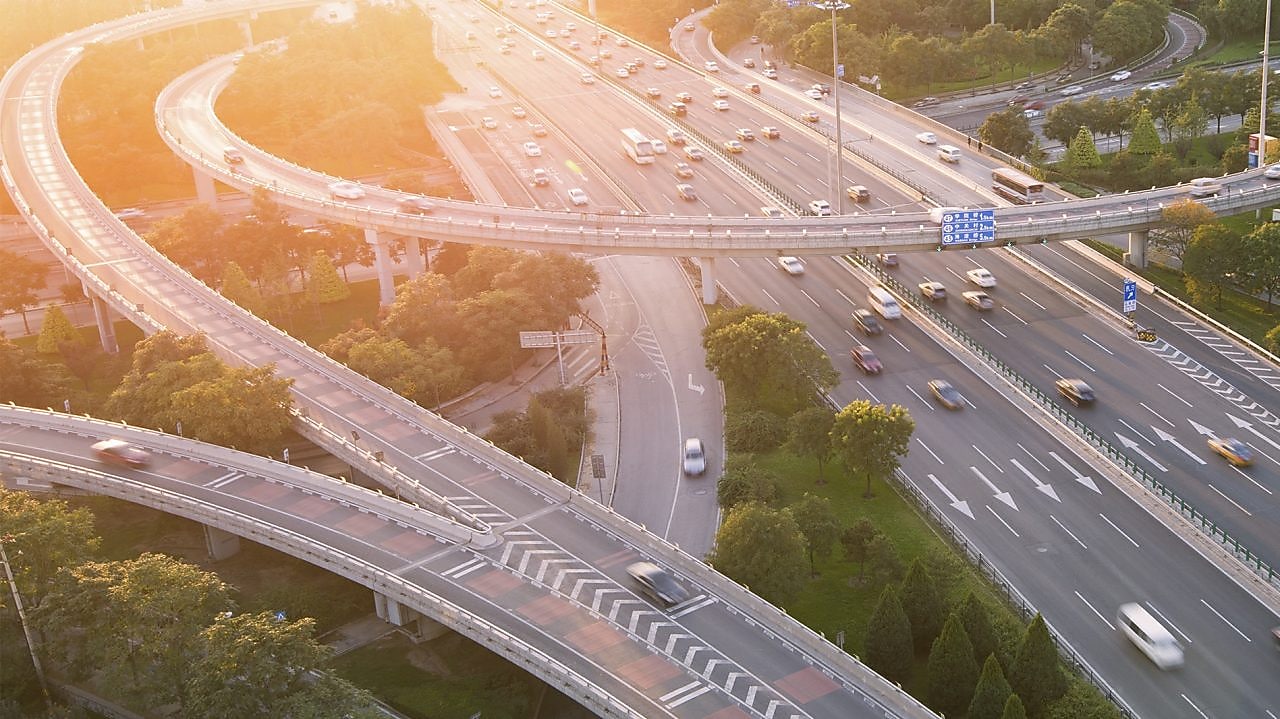 Image of vehicles on motorway/highway with sunset and trees in the background.