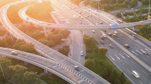 Image of vehicles on motorway/highway with sunset and trees in the background.
