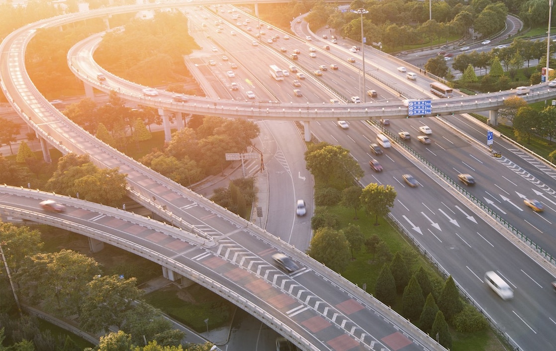 Image of vehicles on motorway/highway with sunset and trees in the background.