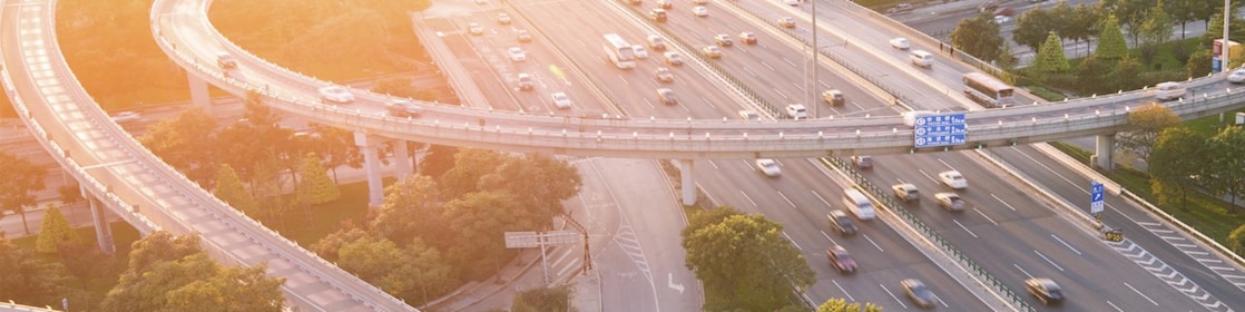 Image of vehicles on motorway/highway with sunset and trees in the background.