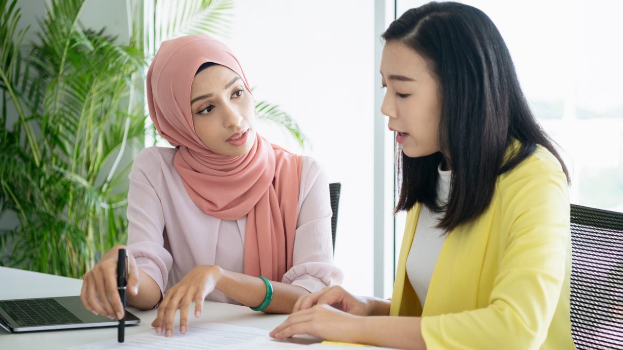 Female inspector discussing with engineer in car factory. Multi-ethnic male and female professionals are standing at car production line. They are in automotive industry.