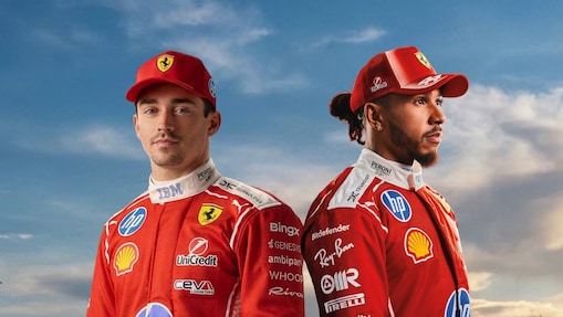 Charles Leclerc and Lewis Hamilton standing side-by-side in their Ferrari F1 racing gears with a blue sky background.