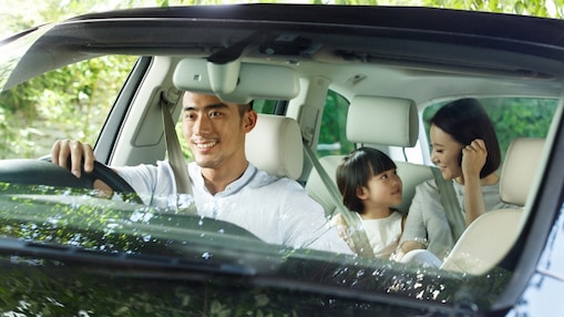 Man driving a black car with a lady and kid at the back seat smiling