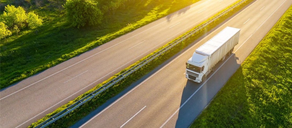 A truck on a highway surrounded by green trees in day time